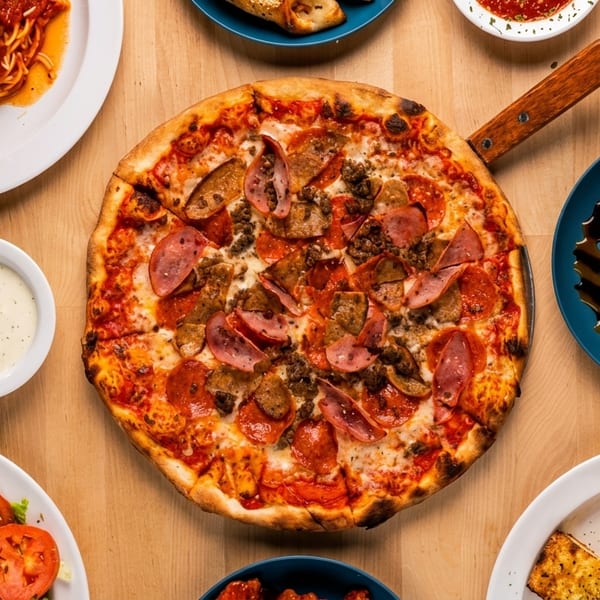 Overhead view of a wooden table laden with various Italian dishes, including pizza, pasta, and salad.