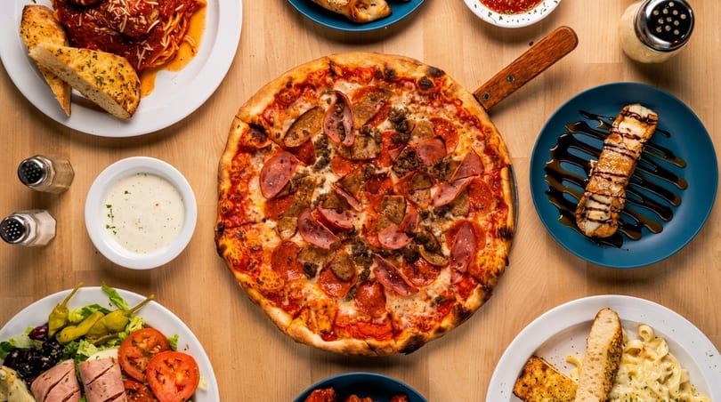 Overhead view of a wooden table laden with various Italian dishes, including pizza, pasta, and salad.
