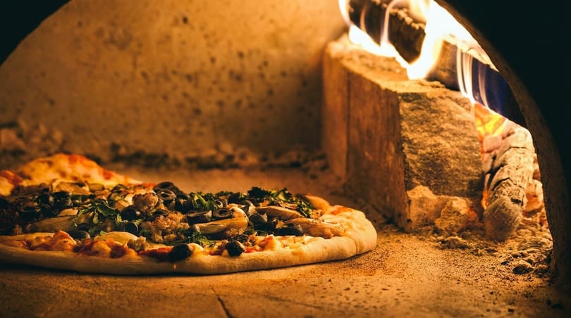 A fresh pizza with various toppings baking inside a wood-fired oven with glowing embers.